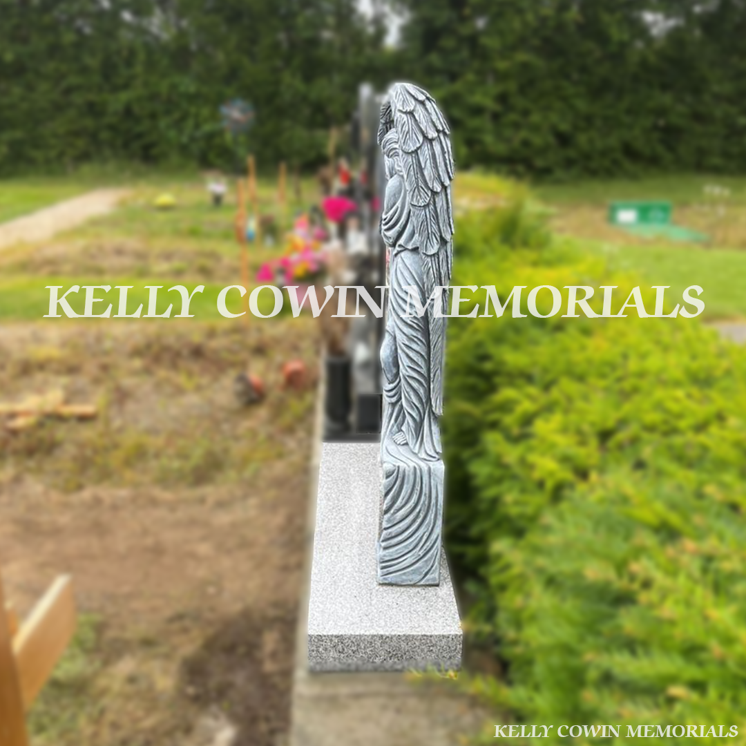 Side view of grey granite angel headstone showing carved wing detail and plinth in Flemington Cemetery Dublin