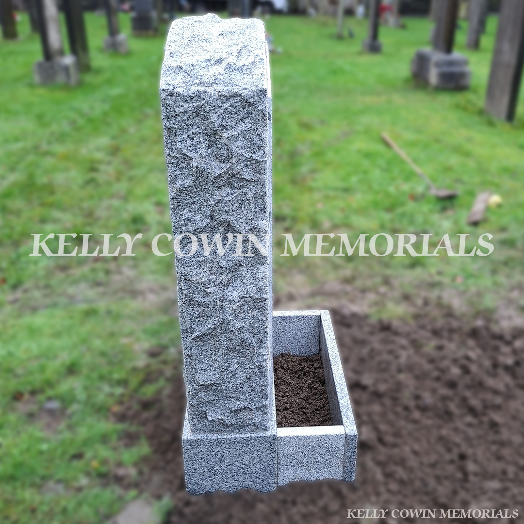 Side view of a Grey granite rough boulder headstone with flower box and black inscription in Glasnevin Cemetery Dublin by Kelly Cowin Memorials