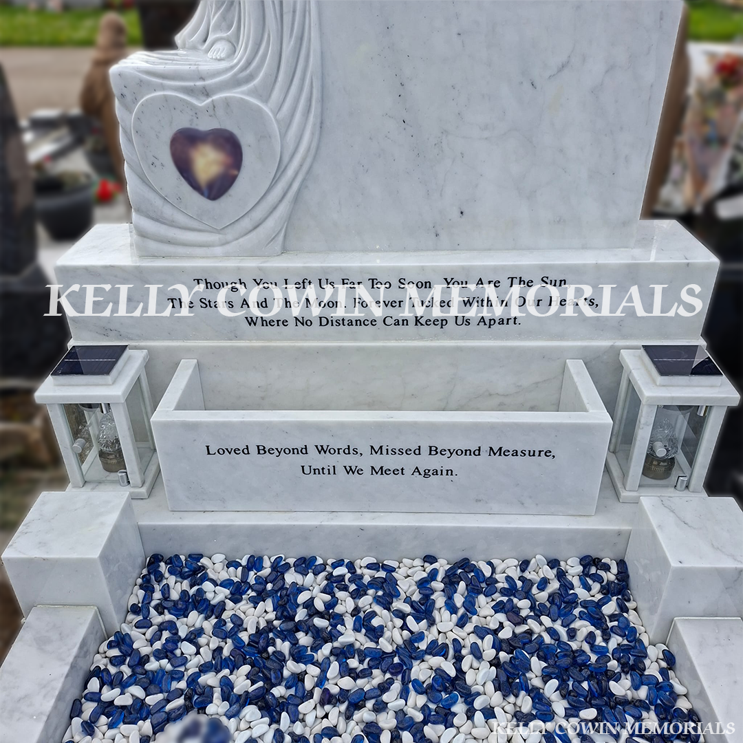 Close-up of angel carving and black inscription on white marble headstone